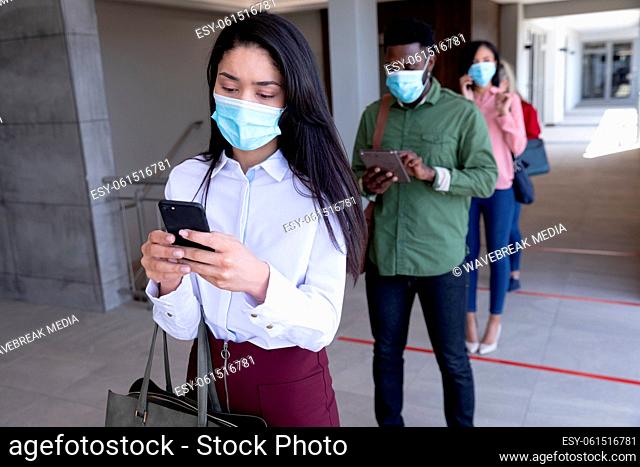 Group of people wearing face masks using smartphones while standing in queue