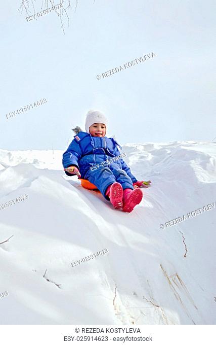 Little girl on a sled sliding down a hill on snow in winter