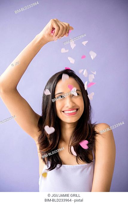 Smiling Mixed Race woman sprinkling heart-shape confetti