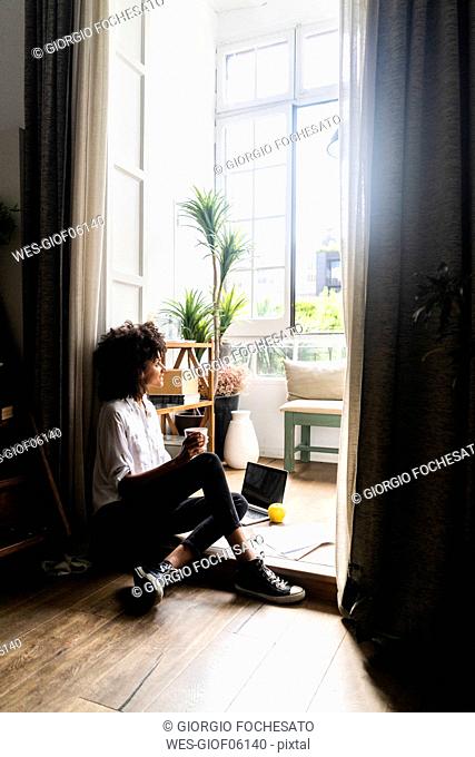 Relaxed woman sitting on floor of her flat, drinking coffee