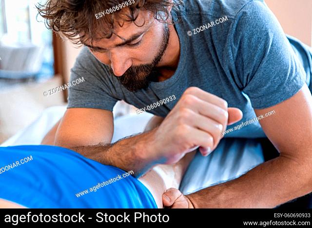 Close-up view of massage therapist giving body massage to sportsman with forearm. Professional masseuse applying pressure with his arm to patient legs