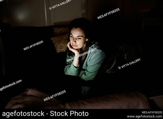 Young woman looking at laptop while lying on bed at home
