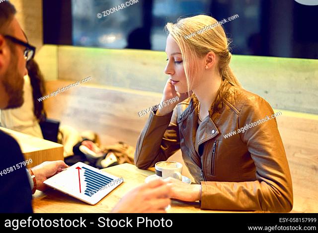 Businessman showing blond woman a business chart on his digital tablet while meeting in a coffeebar