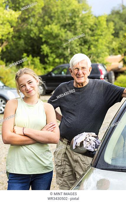 senior grandfather and his 13 year old grand daughter washing a car together in driveway
