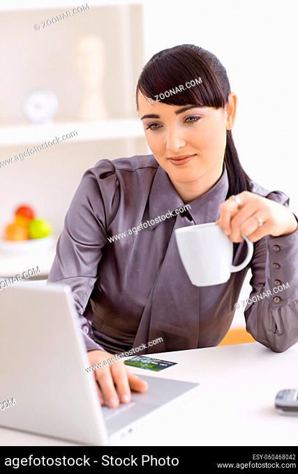 Young woman drinking coffe while shopping online using her laptop