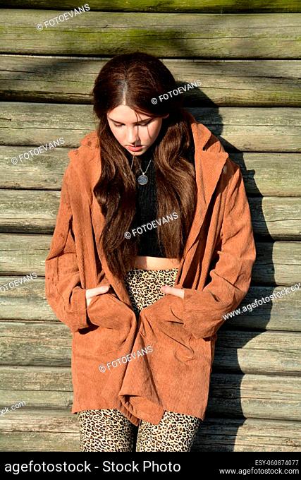 A young woman with a brown coat, posing in front of old wooden planks