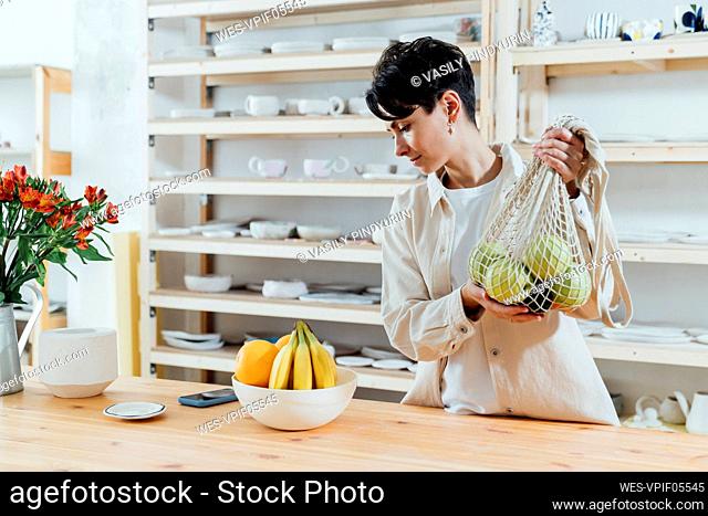 Entrepreneur holding mesh bag of fresh fruit by table