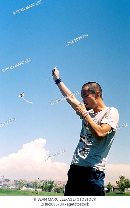 A young man lights a cigarette while flying a bee shaped kite at a Los Angeles State Historic Park just outside of downtown Los Angeles