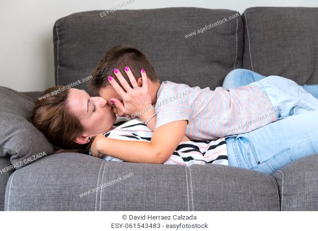 Woman lying on sofa kissing her little son in cheek. Mom with little boy joyfully spending time in cozy living room at home