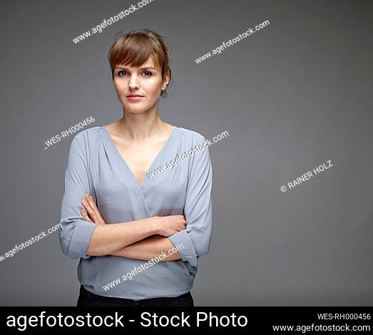 Portrait of young woman with crossed arms in front of grey background