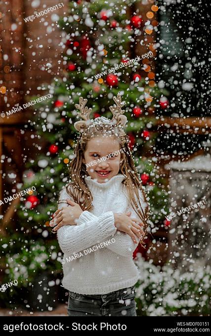 Smiling girl standing under snowfall in front yard