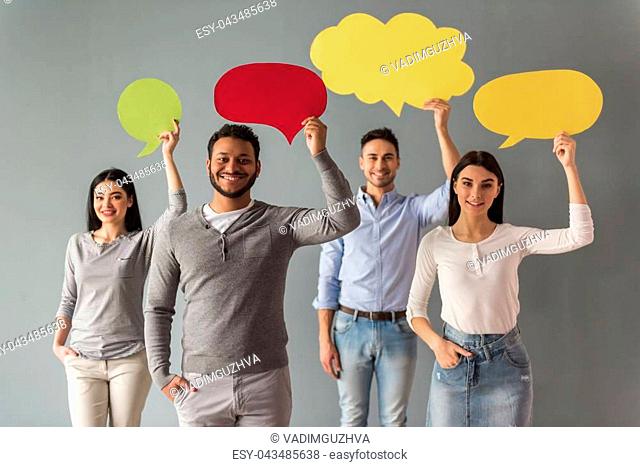Beautiful young people are holding speech bubbles, looking at camera and smiling, on gray background