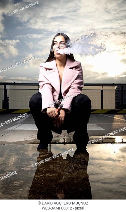 Portrait of fashionable young woman smoking electronic cigarette on parking level