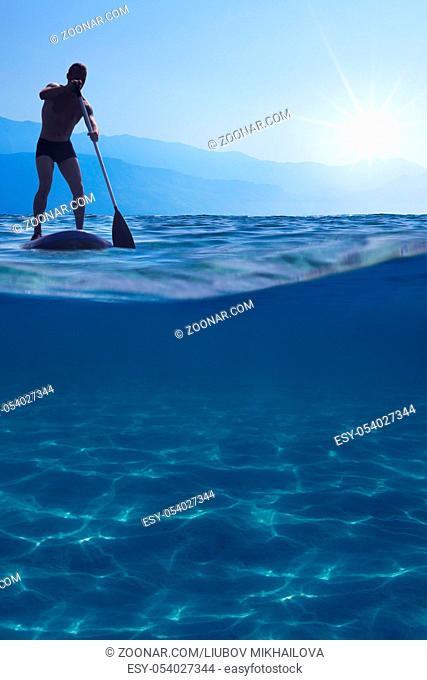 Stand up paddle boarding. Young man floating on a SUP board. Underwater view of sea, copy space for text