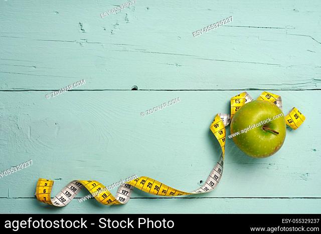 Diet or healthy eating concept image with an apple and a measuring tape on a rustic wooden table