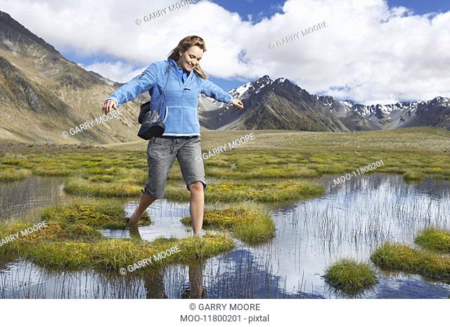Woman walking barefoot through pond by mountains