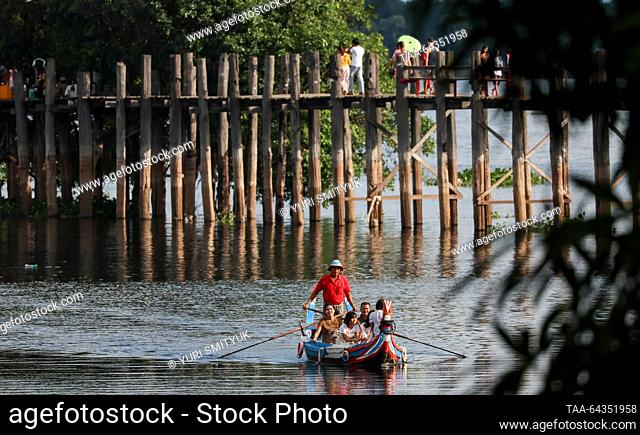 MYANMAR, AMARAPURA - OCTOBER 25, 2023: A boat with tourists is seen by the U Bein Bridge spanning Lake Taungthaman. The 1