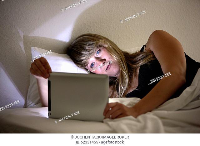 Young woman lying in bed surfing the internet on an iPad, tablet computer with wireless internet access