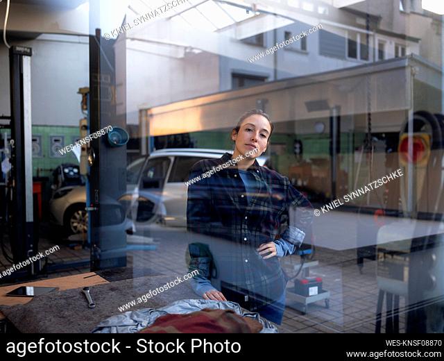 Female mechanic standing at car repair shop seen through window