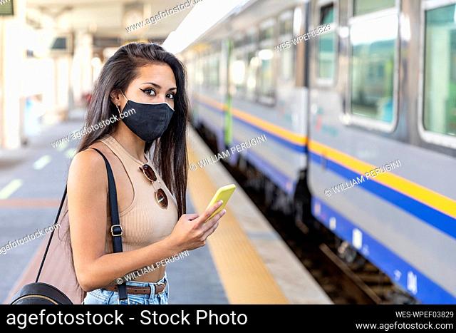 Young woman wearing face mask using mobile phone while standing on platform