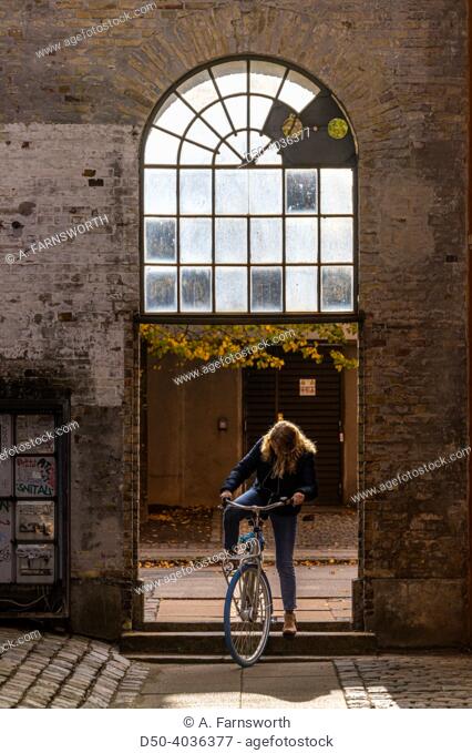 Copenhagen, Denmark A woman cyclist maneuvers a bicycle over a astoop on Reffen island under an arched passageway