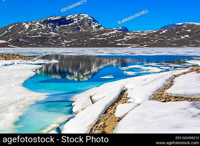 Frozen turquoise lake Vavatn panorama in summer landscape and mountains with snow in Hemsedal Norway
