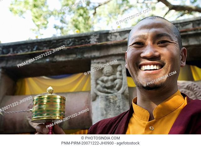 Monk holding a prayer wheel and smiling, Mahabodhi Temple, Bodhgaya, Gaya, Bihar, India
