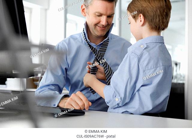 Son putting tie on father at desk
