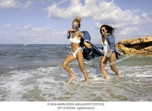Two women running in sea water at beach, Chersonissos, Crete, Greece