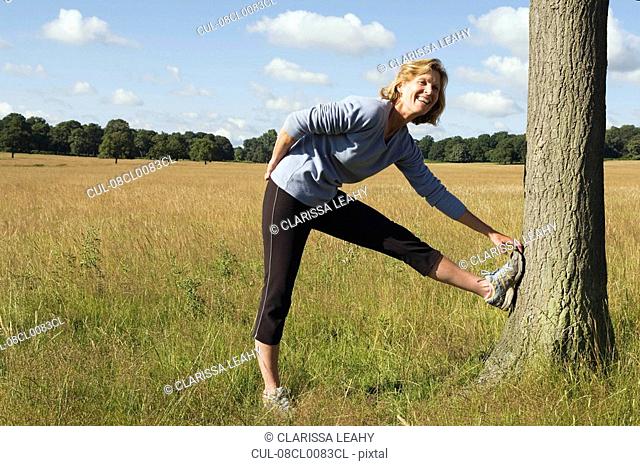 Woman runner stretching against tree