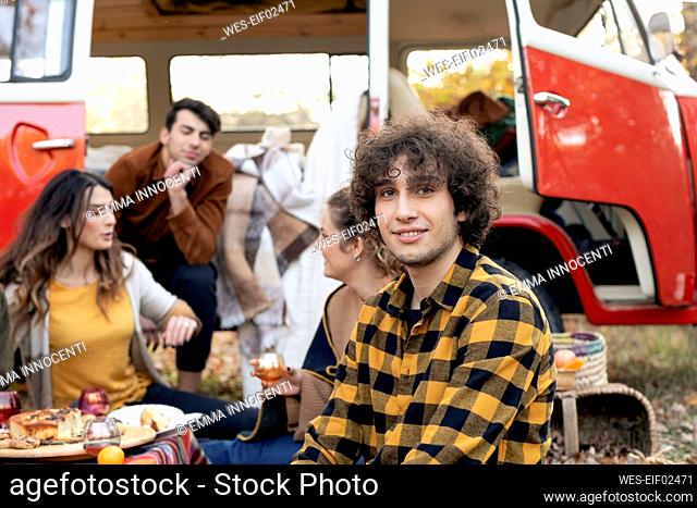 Smiling man with friends talking outside van on picnic