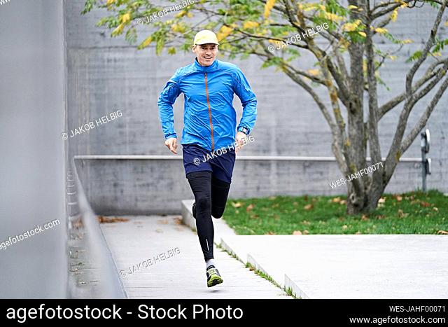 Mature man wearing cap jogging on footpath