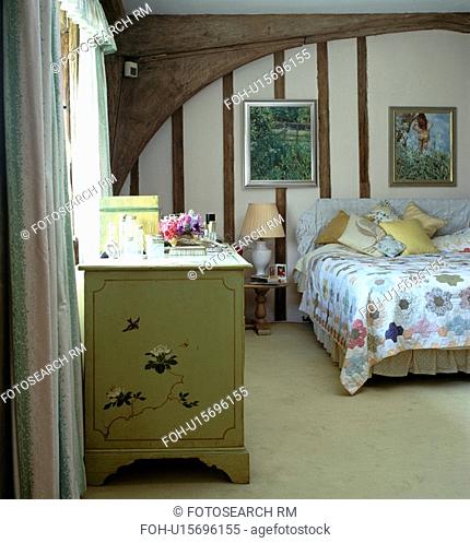 Cream carpet and chest of drawers in country bedroom with beamed walls and patchwork quilt on bed