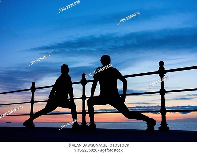 Male and female joggers stretching at sunrise at Seaton Carew on the north east coast of England, United Kingdom