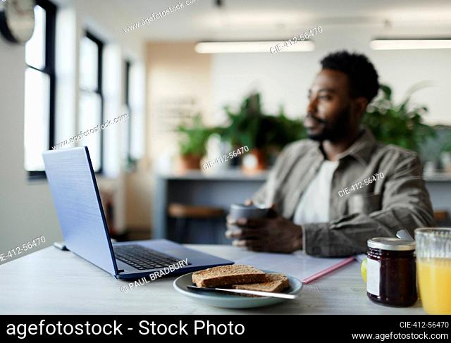 Thoughtful businessman drinking coffee at laptop in office