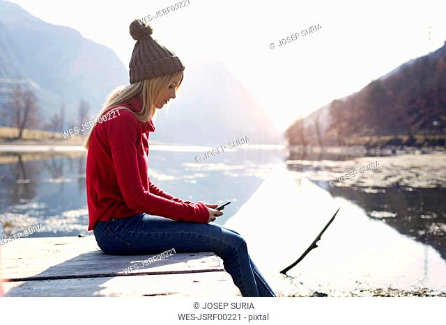 Young blond woman sitting on jetty at a lake in winter