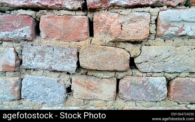 Brick wall. Ceramic brickwork or fence. Old, uneven brick, covered in some places with moss. Texture of crumbling stone with moss and mold