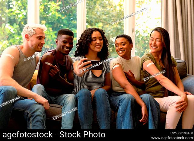 Group of happy diverse female and male friends showing plasters after vaccination and taking selfie