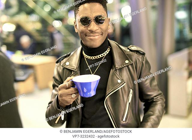 young content fancy man holding coffee cup and smiling, African descent, in Munich, Germany