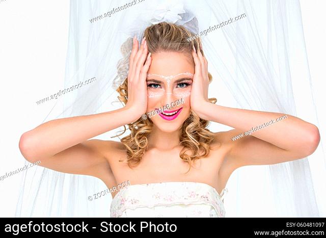 Beautiful young woman in wedding gown with make-up and mask drawn around eyes. surprised expression. Bride with big white bow on head