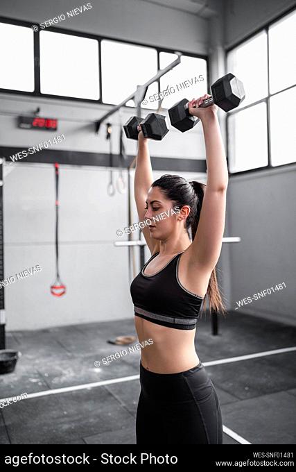 Active woman exercising with dumbbells in gym