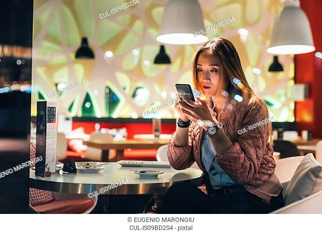 Woman sitting in restaurant, using smartphone