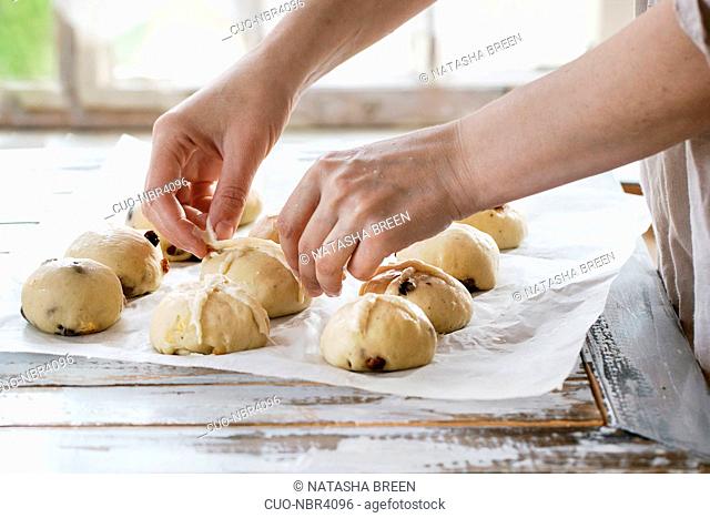 Raw unbaked buns. Ready to bake homemade Easter traditional hot cross buns on baking paper over white wooden table. Window at background