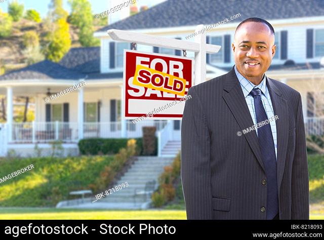 African american agent in front of beautiful custom house and sold for sale real estate sign