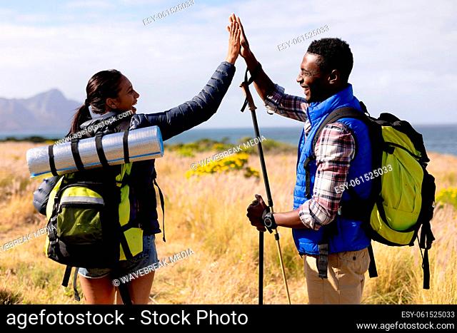 Fit african american couple wearing backpacks high fiving hiking on coast