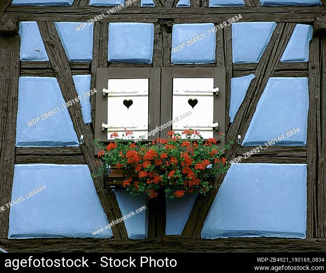 Window of blue-half-timbered house with closed shutters carved with hearts