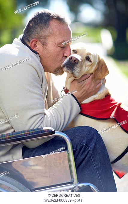 Man in wheelchair kissing dog in park