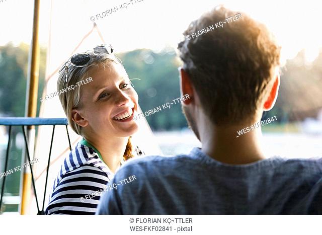 Young woman laughing at man at a lake next to sailing boat