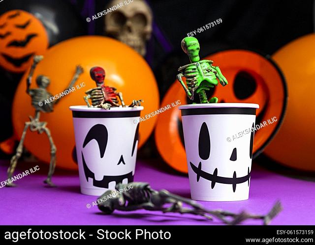 Halloween party. Skeletons coming out from the cup with balloons and skull in the background