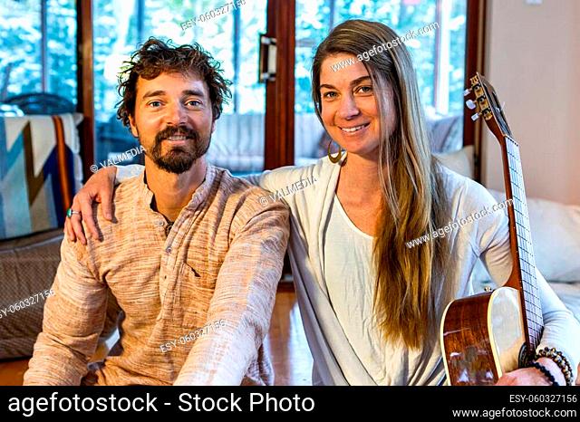 Happy shamanic man and woman in room holding musical instruments like classical guitar looking at camera while preparing for calm peaceful meditation